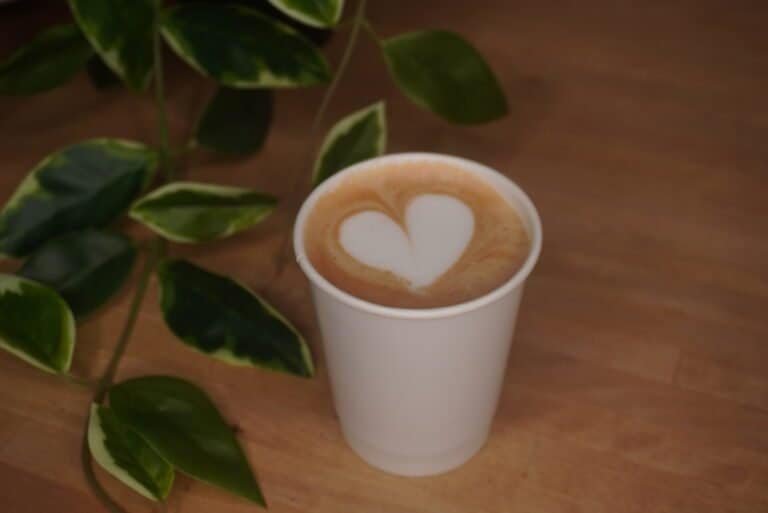 Latte with heart-shaped foam art in a white cup on a wooden table.