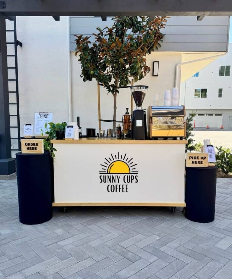 Sunny Cups Coffee outdoor stand with coffee equipment and trees.