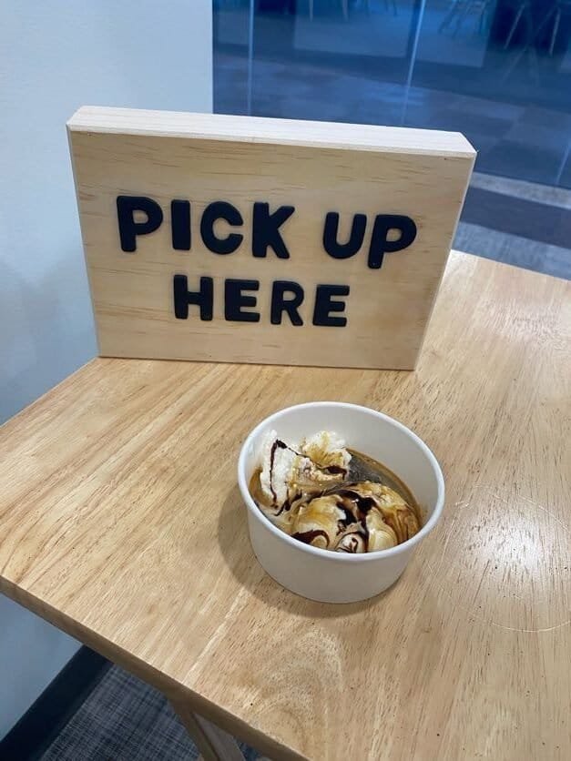 Pick Up Here sign on a wooden board at Sunny Cups Coffee.