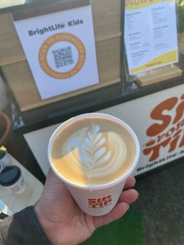 Coffee art latte in a Sunny Cups Coffee cup at an outdoor location.