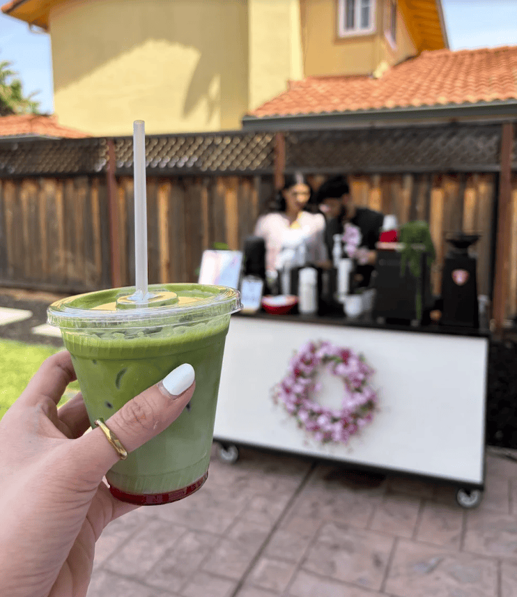 Fresh Matcha Latte in a clear cup with a straw, held by a person with white nail polish.