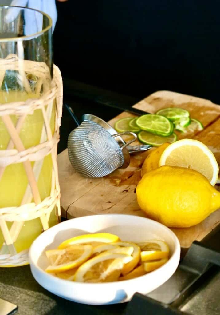 Lemonade with fresh lemon slices and lime wedges on a wooden cutting board.