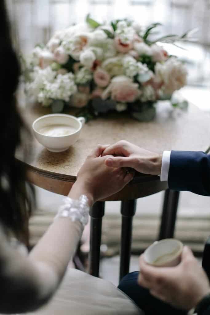 Wedding couple holding hands at a table with coffee and flowers.