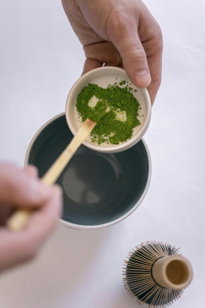 Matcha powder being sifted into a cup for a vibrant green tea.