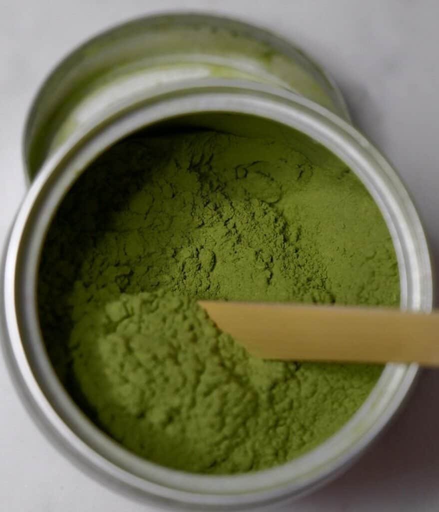 Fine green matcha powder in a jar with a wooden scoop.