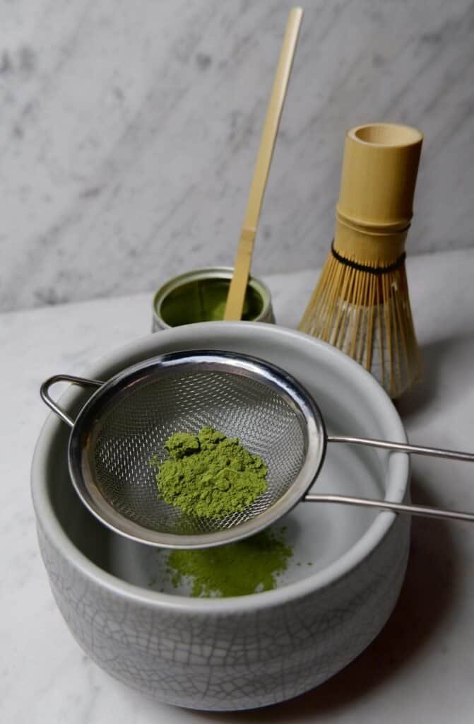 Matcha powder being sifted into a bowl for tea preparation.